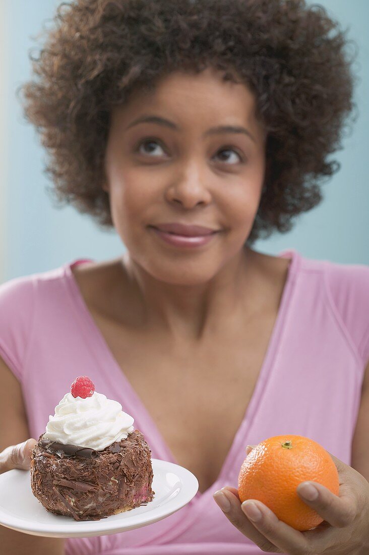 Young woman undecided between cake and orange