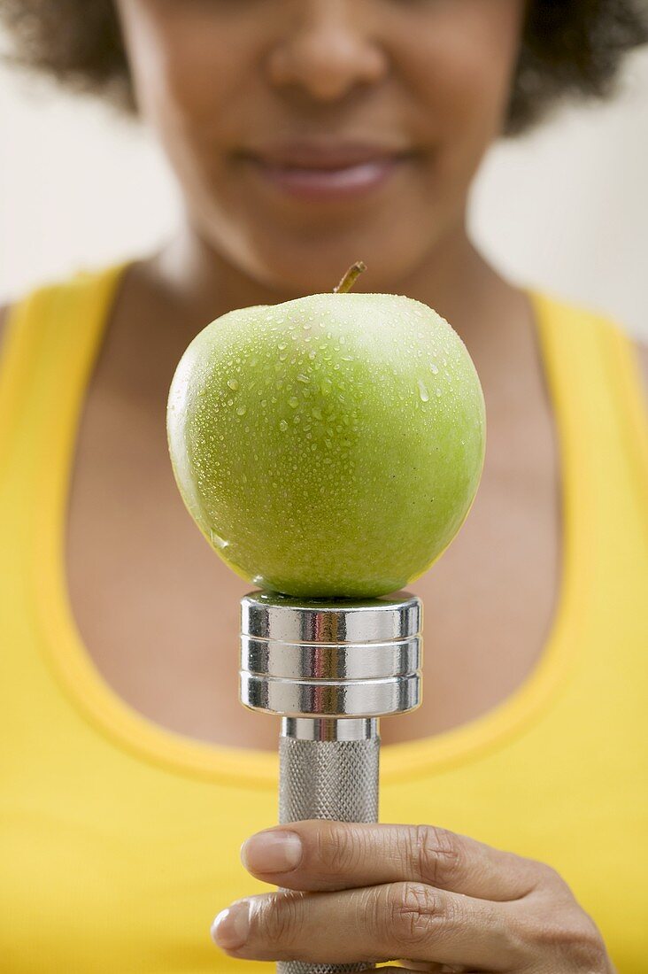 Young woman balancing a fresh apple on a hand weight