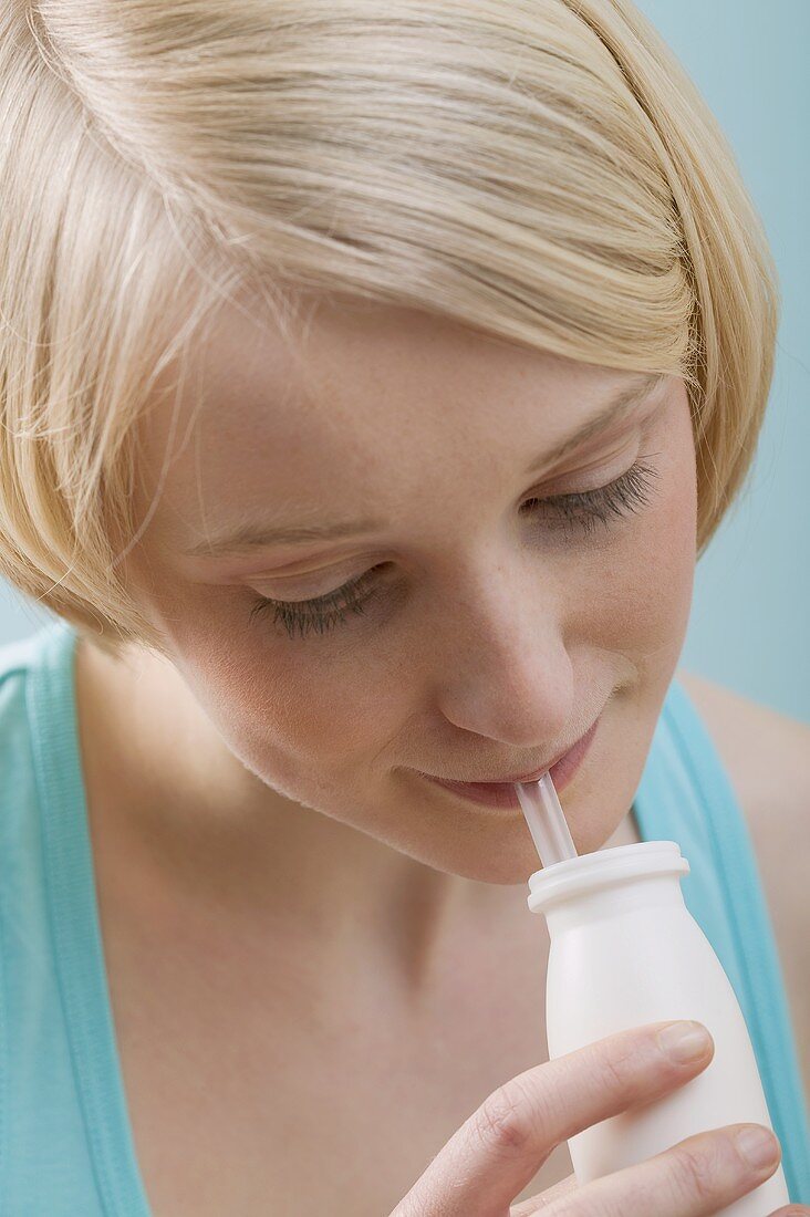 Junge, blonde Frau trinkt mit Strohhalm aus Plastikflasche
