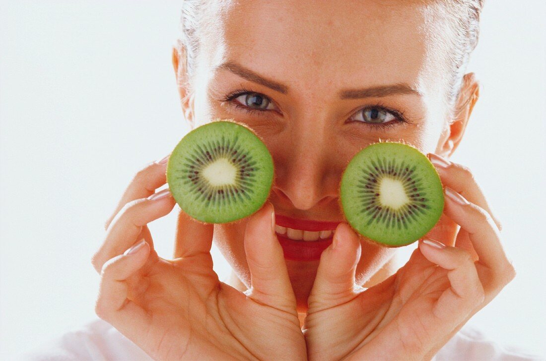 Woman with two halves of kiwi fruit