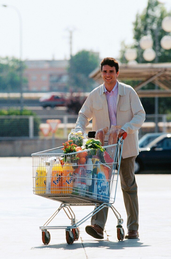 Mann beim Einkauf mit Einkaufswagen auf Parkplatz