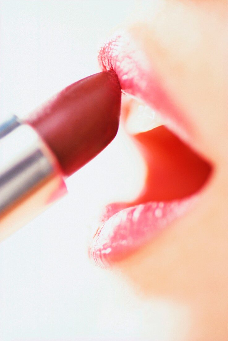 Woman applying lipstick with open mouth