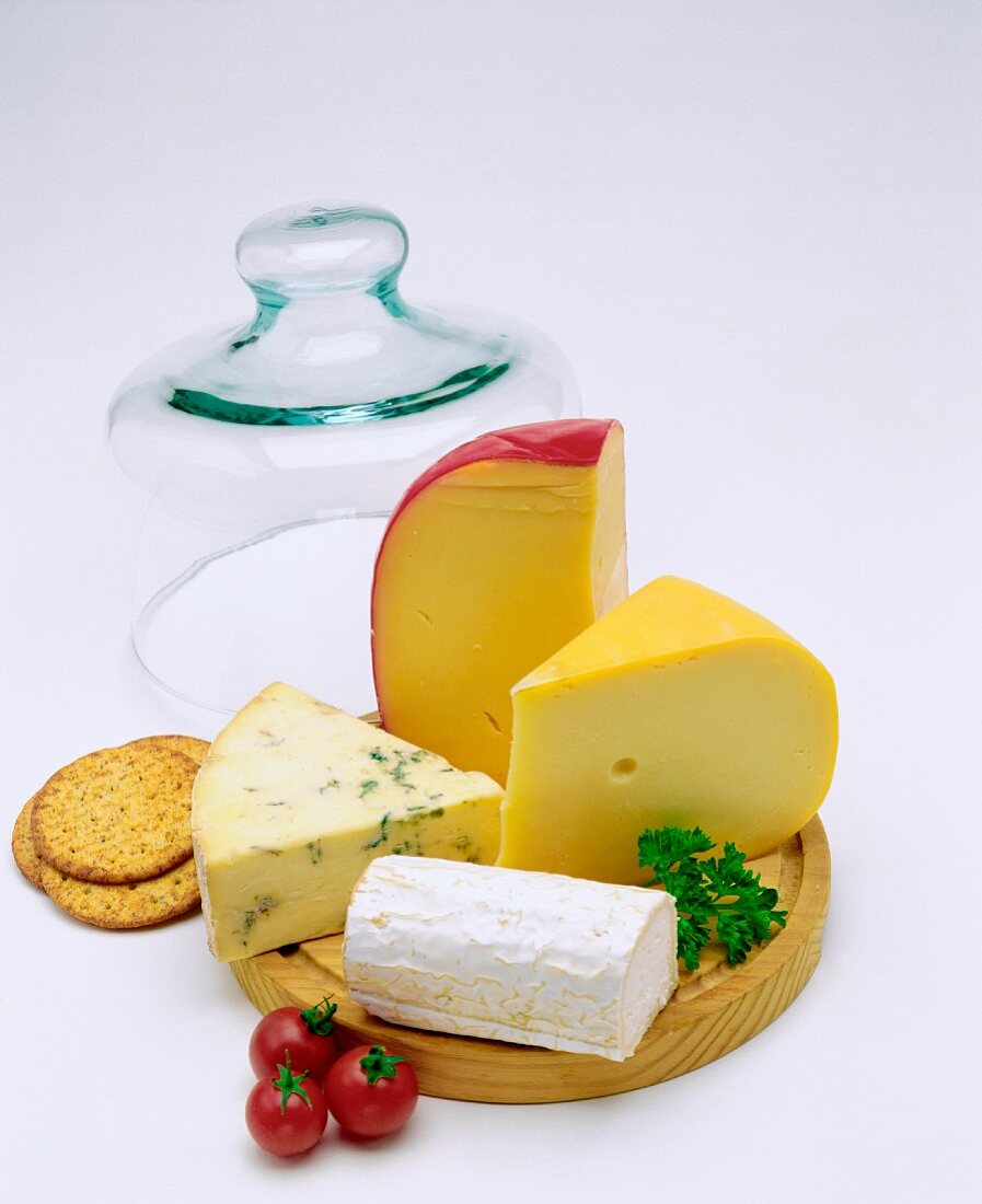 Cheeseboard of various cheeses with glass cheese cover in background