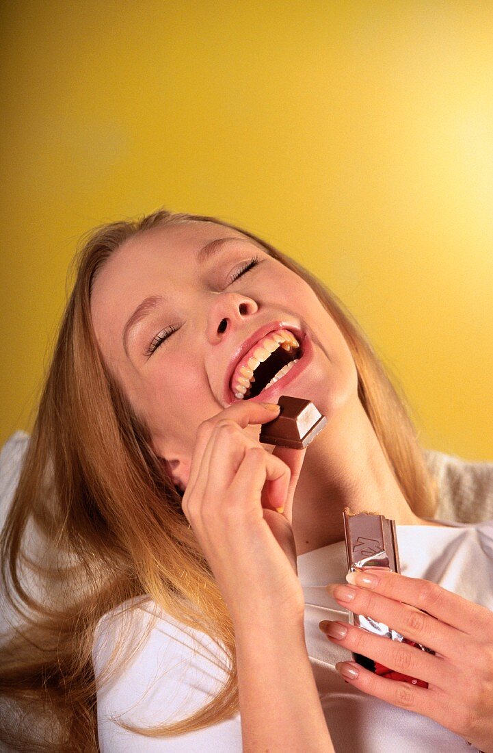 Glückliche, lachende Frau isst einen Schokoriegel