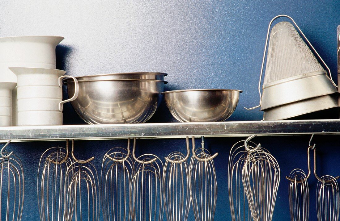 A kitchen shelf with egg whisks and bowls