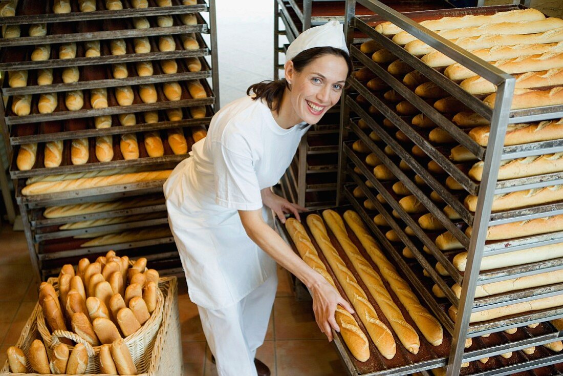 Baker in bakery with trays of baguettes