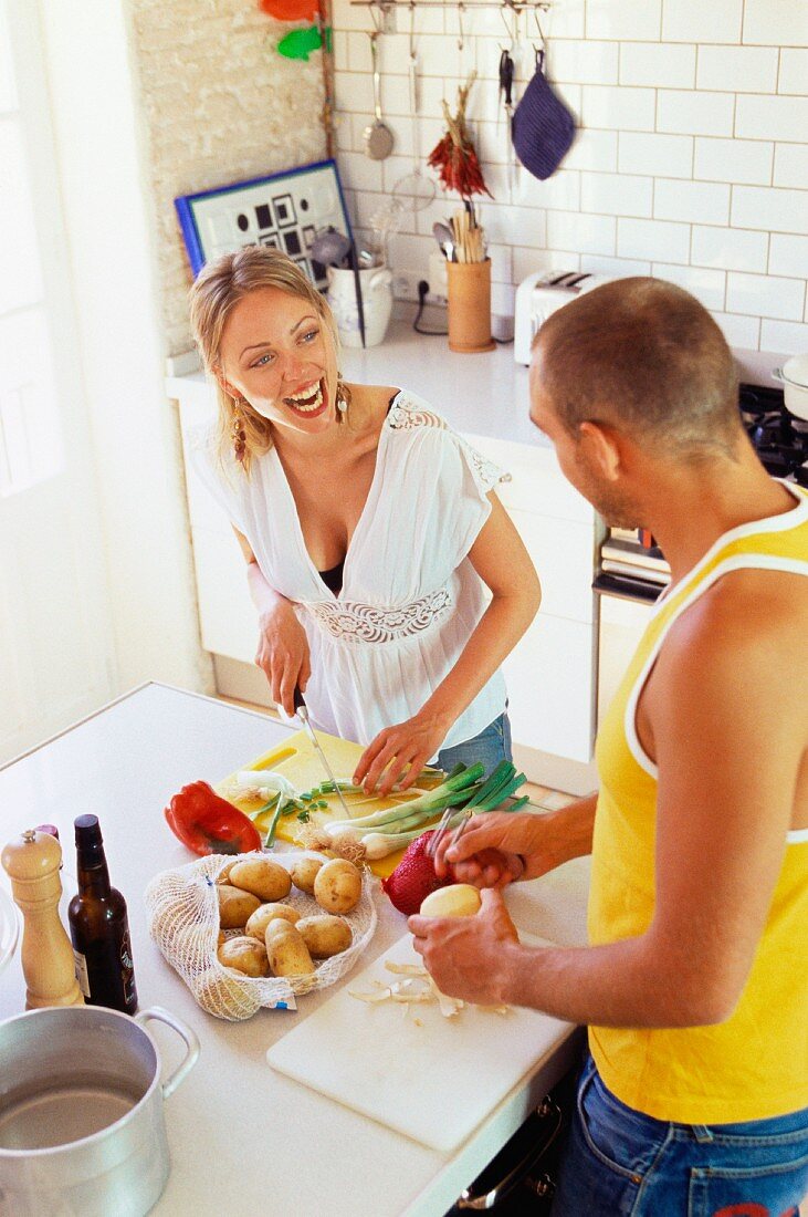 Couple in kitchen peeling potatoes and chopping vegetables