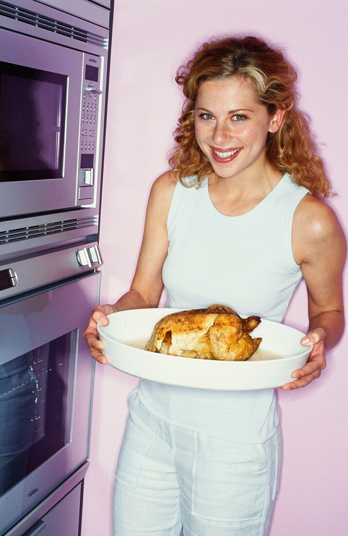 Frau mit einem Grillhähnchen in der Küche