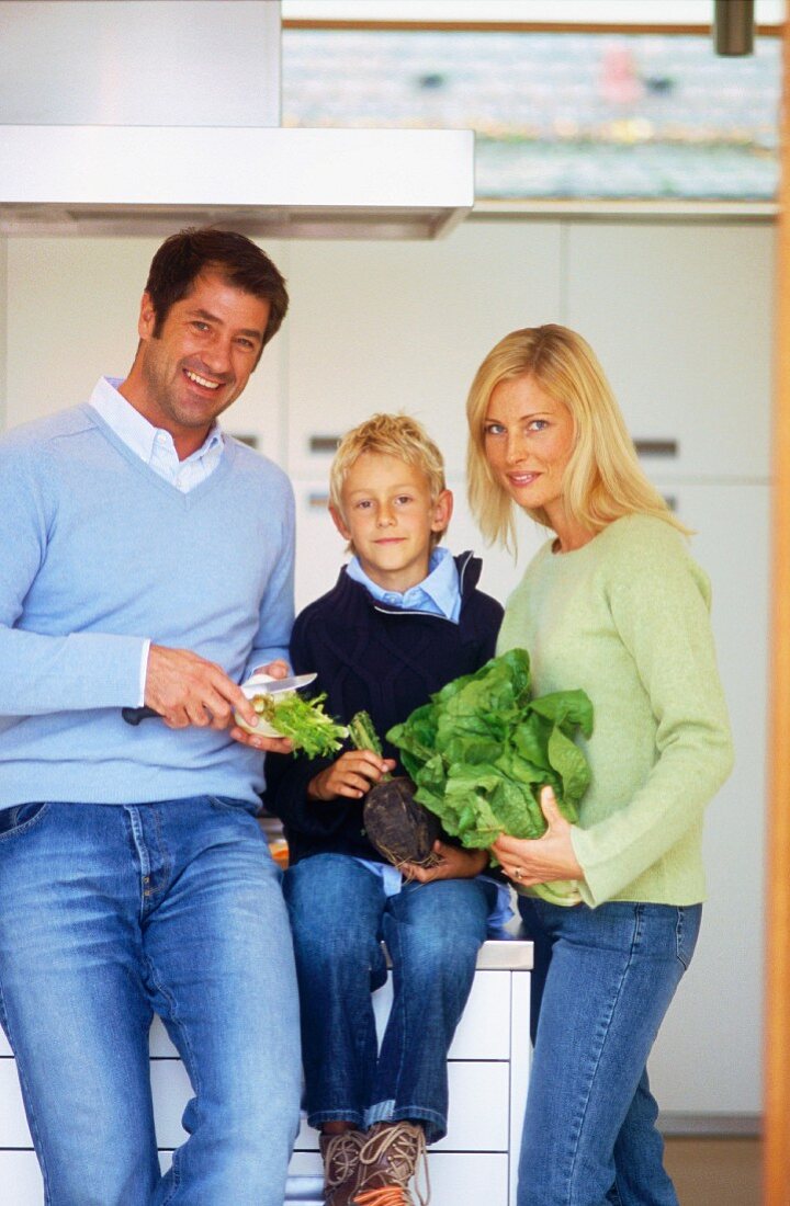Vater, Mutter und Sohn mit Salat und Gemüse in der Küche