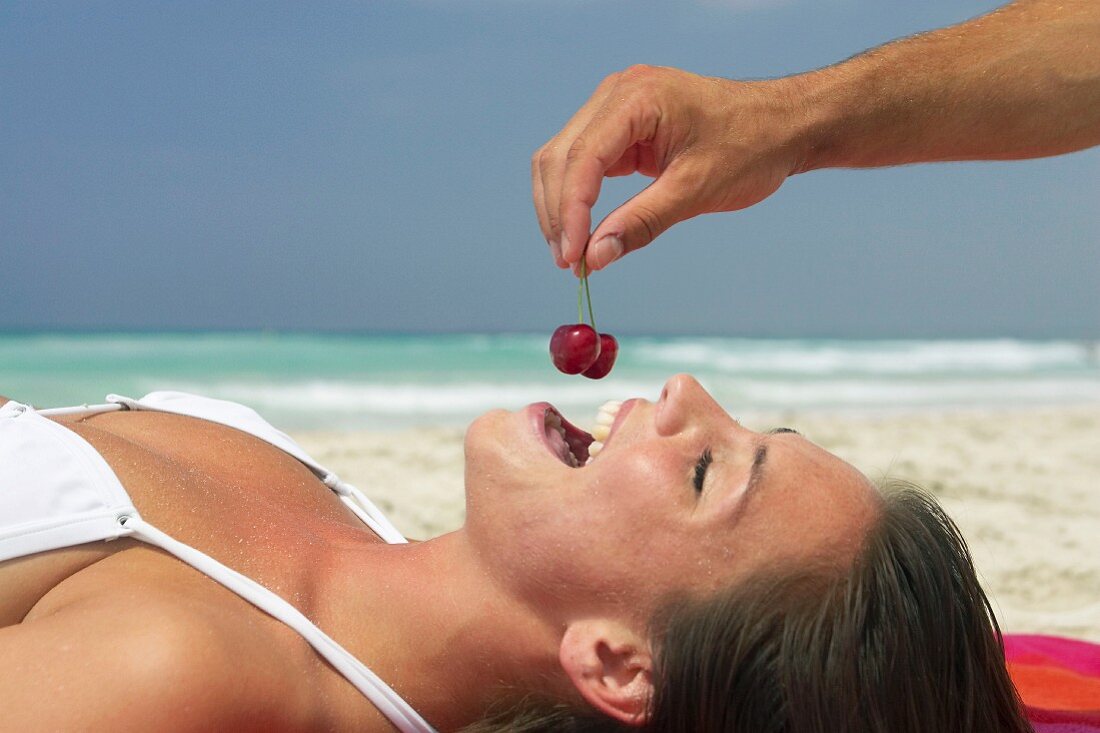 Woman being fed cherries on beach