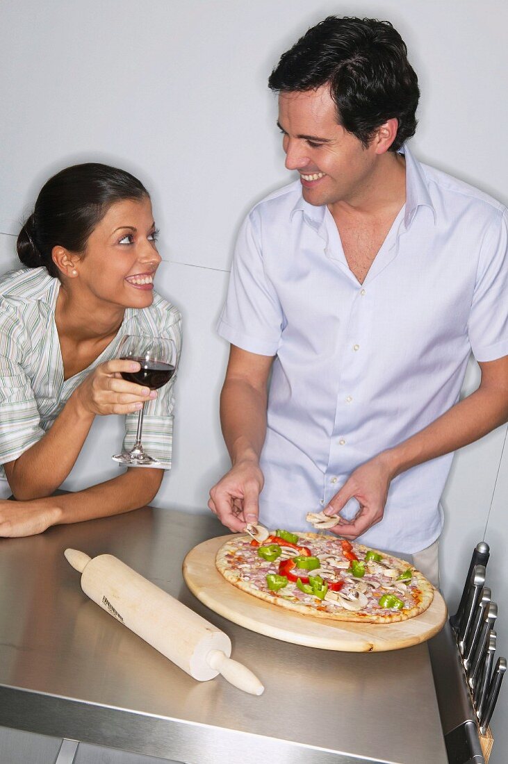 Couple topping a pizza in kitchen