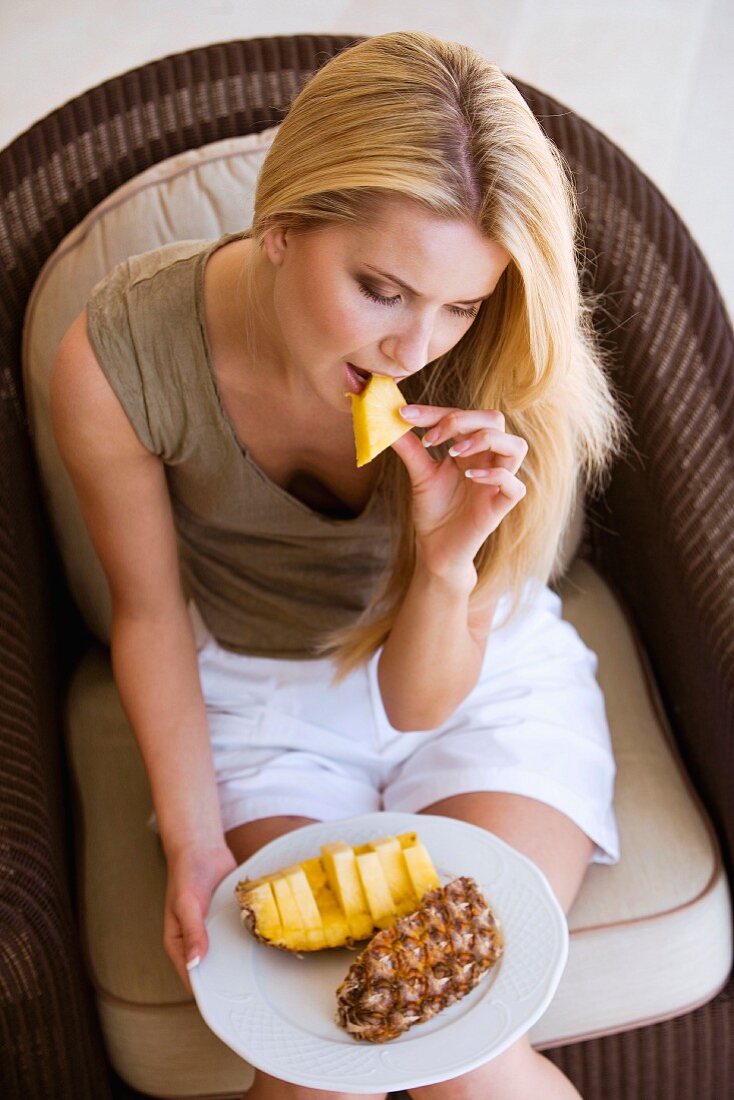 Blond woman, seated, eating a pineapple