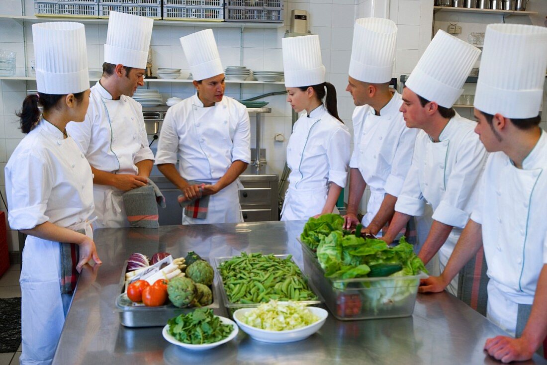 Trainee chefs learning to cook from a head chef in a commercial kitchen