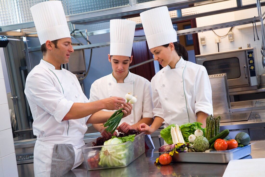 Three chefs preparing vegetables in a commercial kitchen