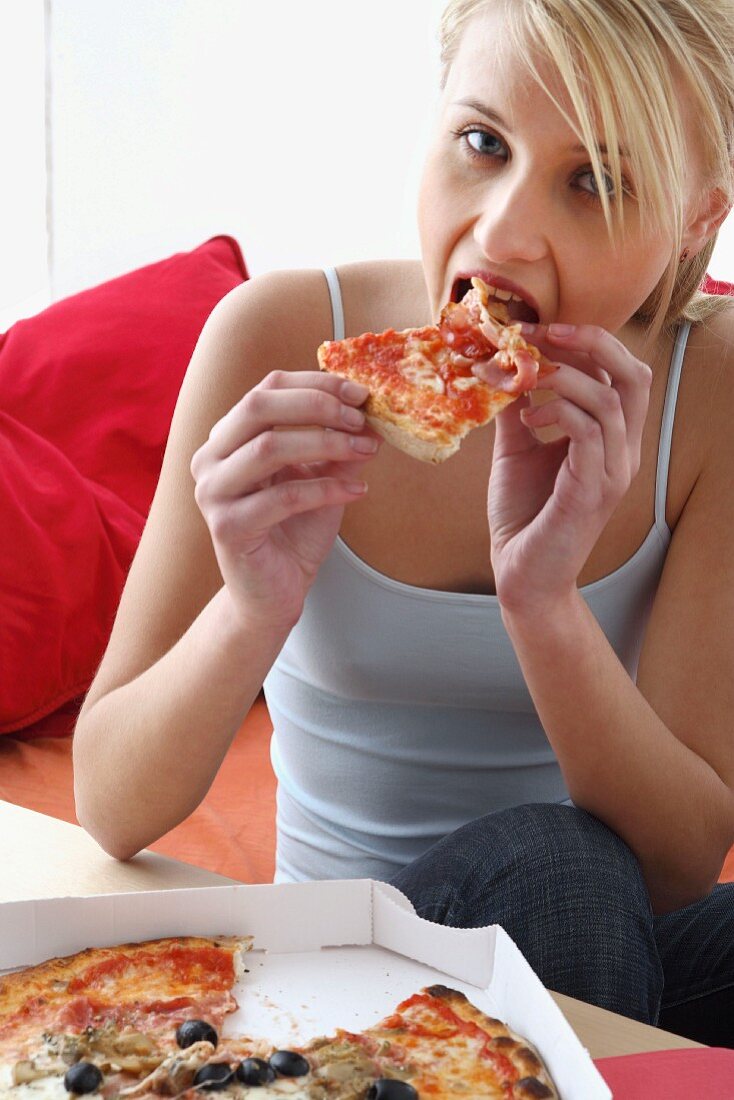 Frau isst Pizza aus Pizzaschachtel im Sitzen
