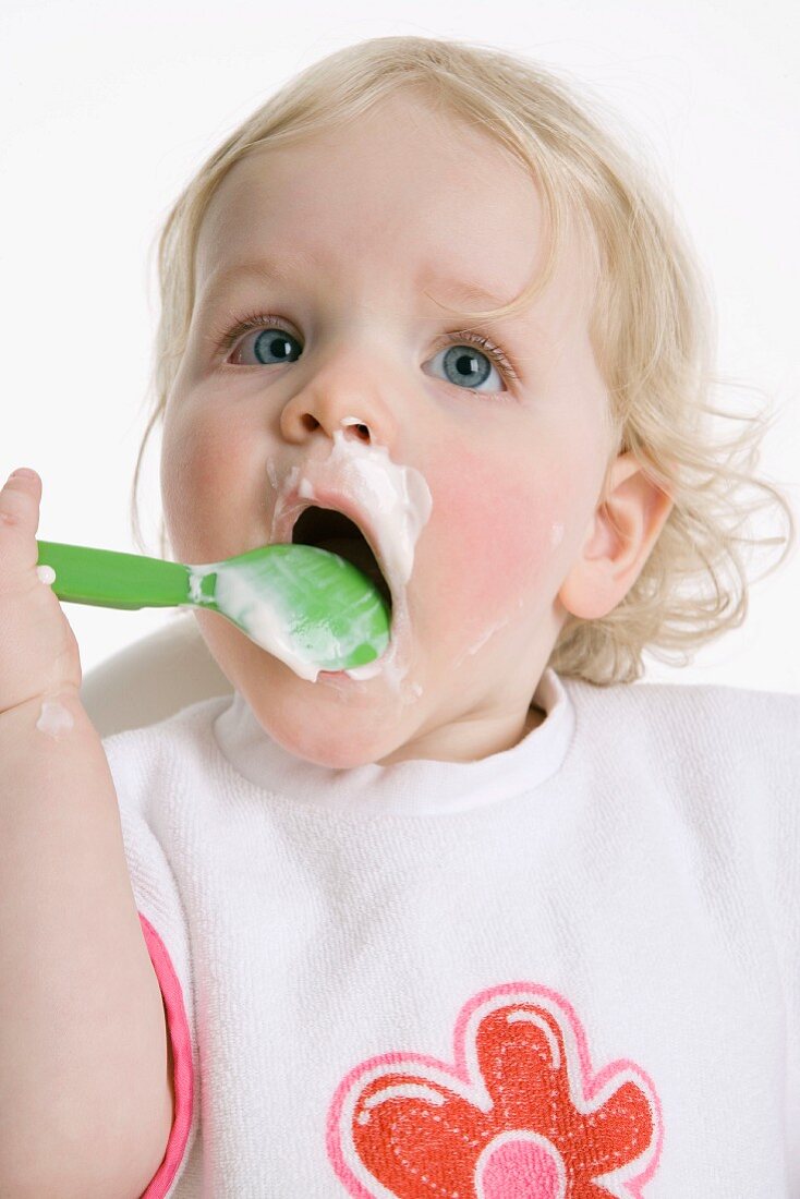 Little girl eating mush from plastic spoon