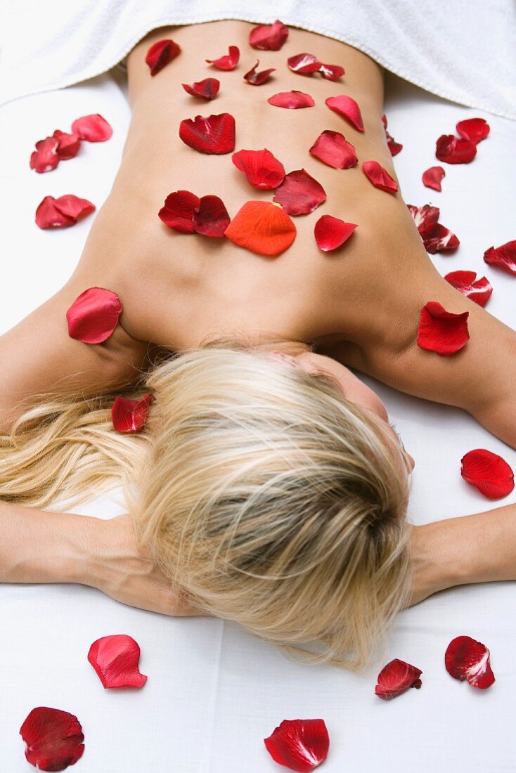 Prone, blonde woman with rose petals scattered on skin