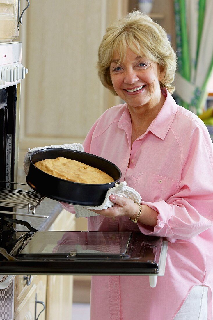 Ältere Frau beim Kuchen backen neben Backofen