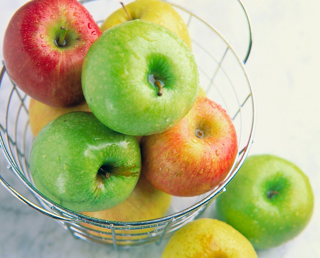 Three types of fresh apple in a wire bowl