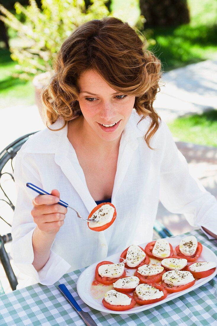 Frau isst Mozzarella mit Tomaten