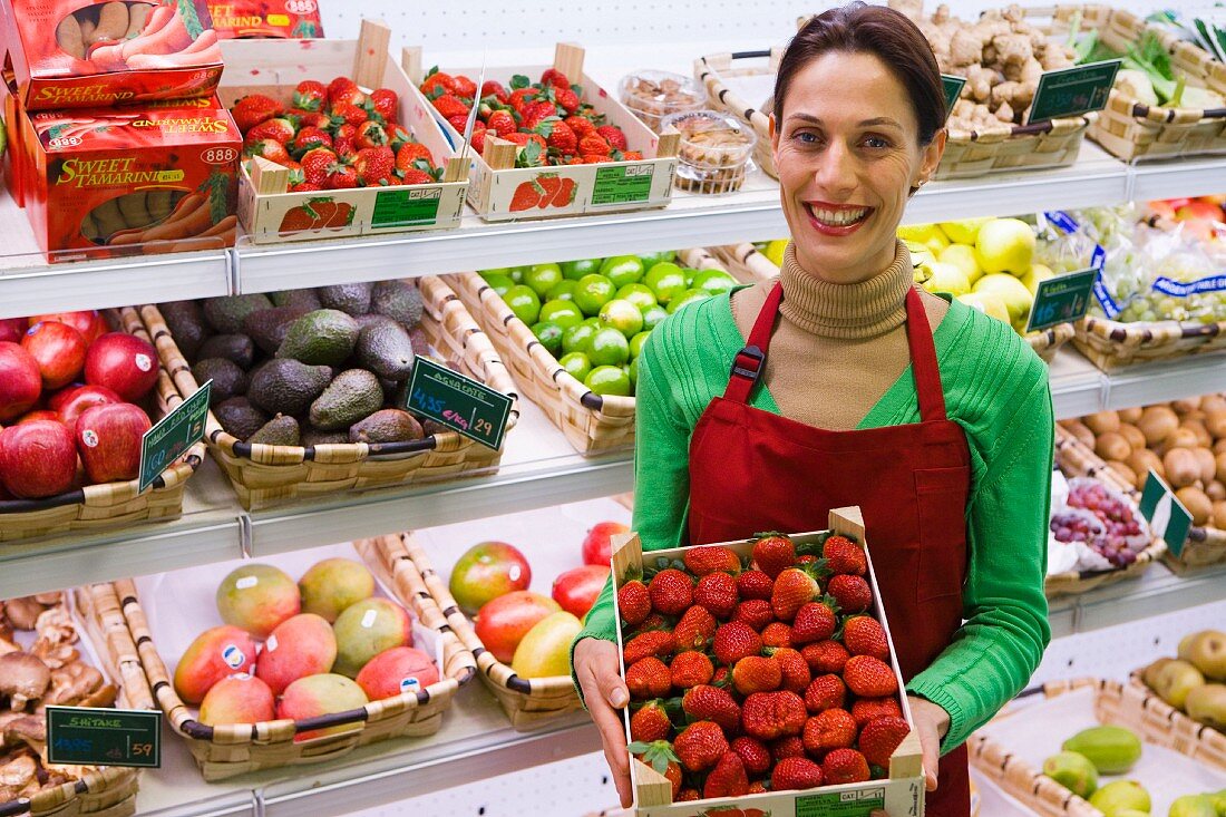Verkäuferin vor Obstregal mit einer Steige Erdbeeren