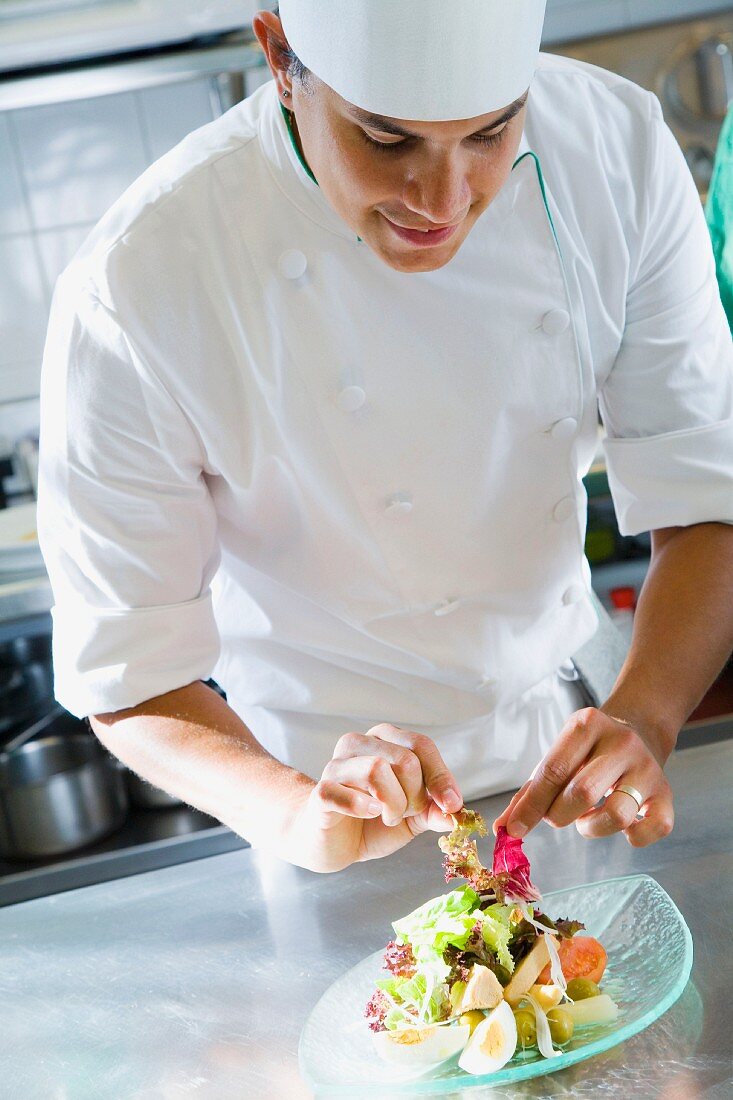 A chef in a commercial kitchen preparing a salad