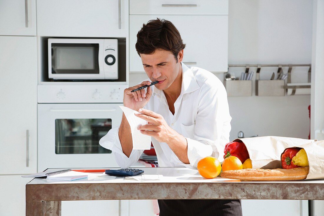 Man in kitchen with shopping calculating household budget