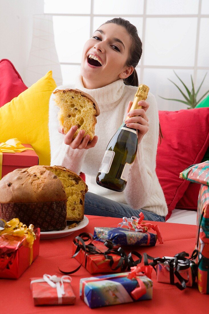 Frau an Weihnachten hält ein Stück Panettone & Flasche Sekt