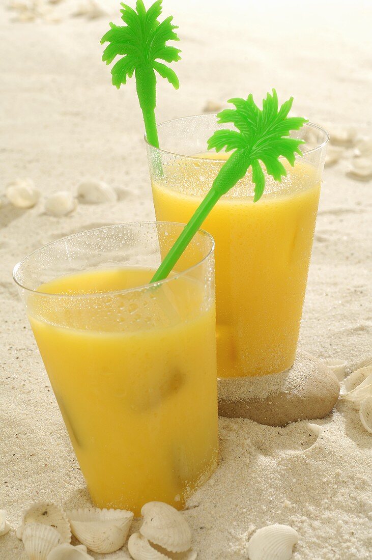Two glasses of orange juice in sand