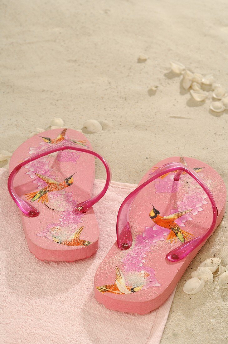 Pinke Flip-Flops auf Handtuch im Sand