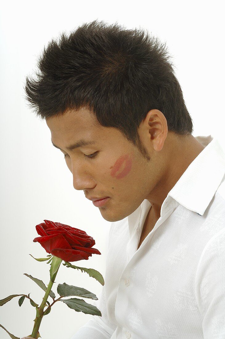 Asian man with red rose and lipstick on cheek