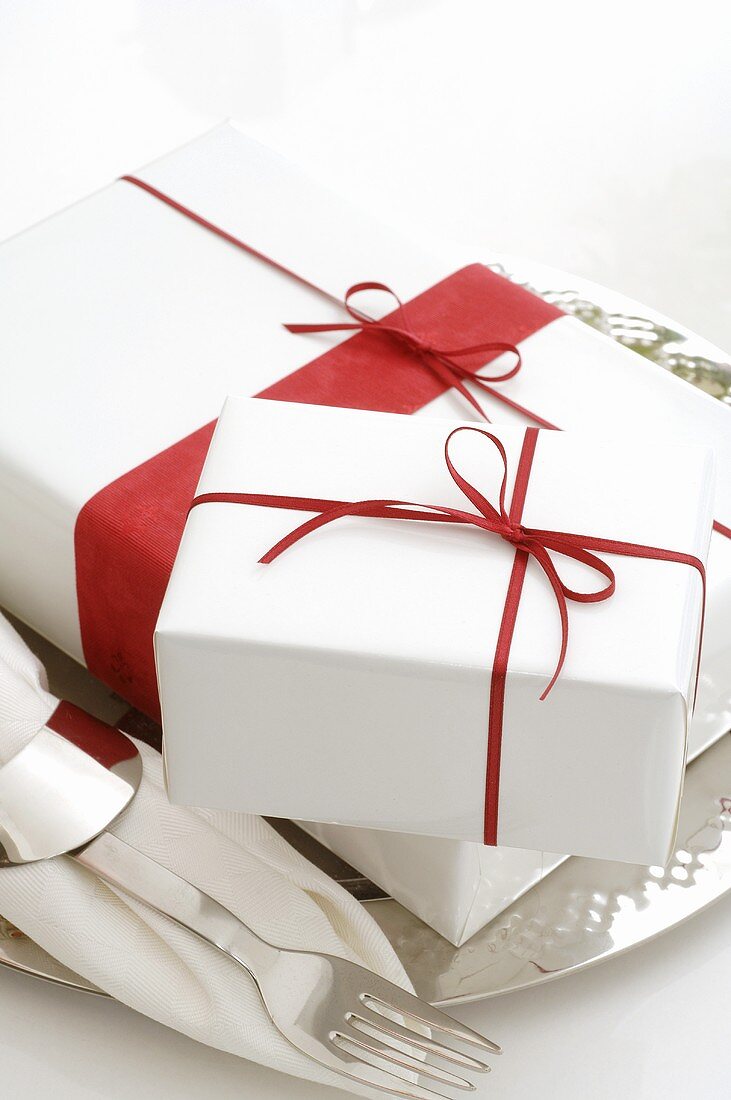 Gifts in white wrapping paper with red bows on silver plate