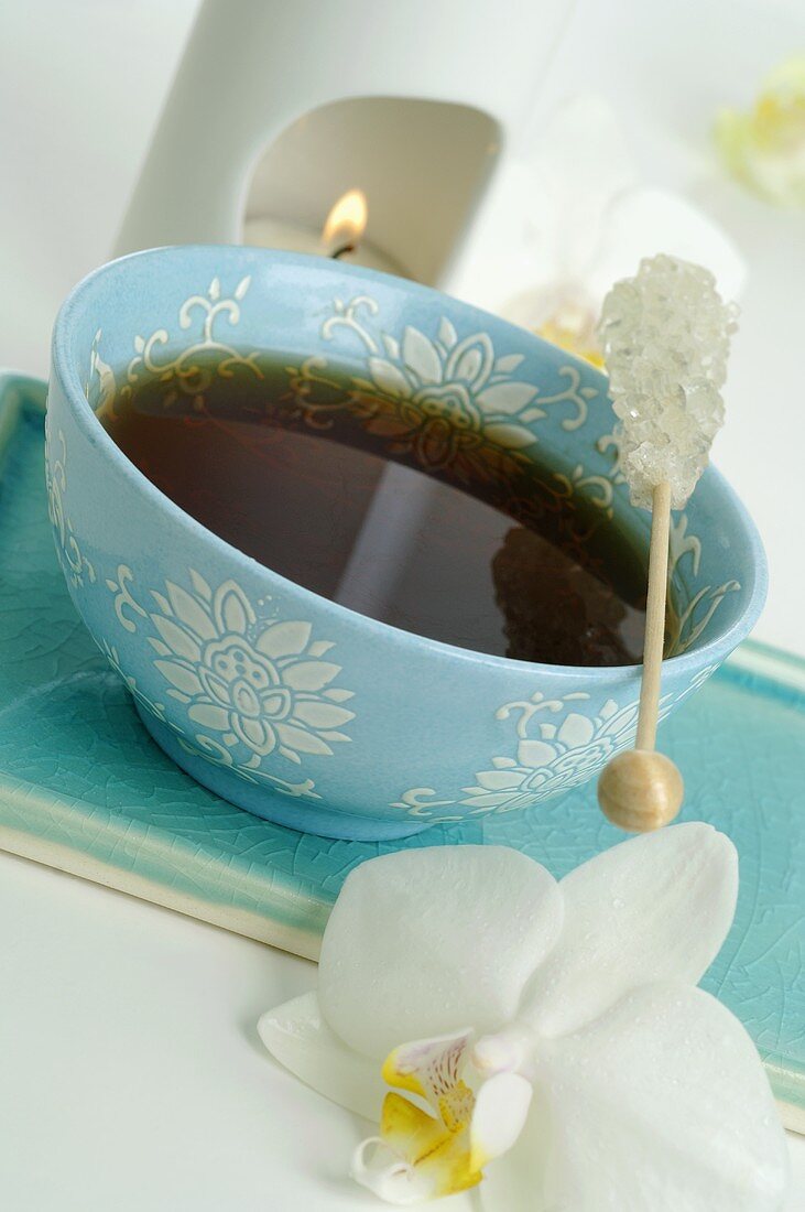 Cup of tea with sugar swizzle stick, aroma lamp, orchid