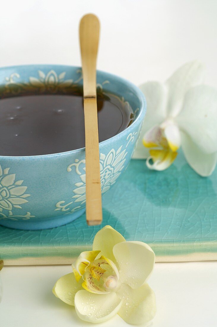 Bowl of tea with wooden spoon, orchid flowers beside it