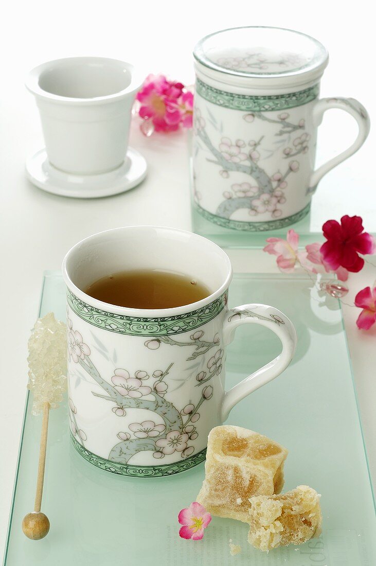 Tea in two Asian mugs, rock sugar, flowers