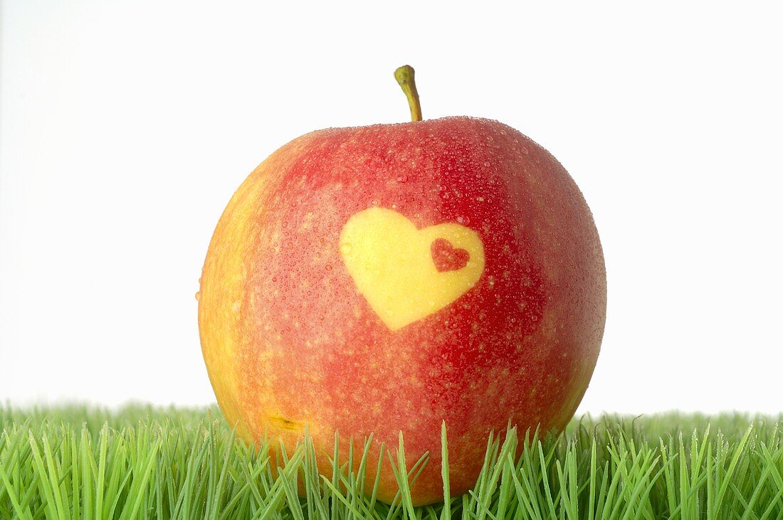Roter Apfel mit Herz im Gras