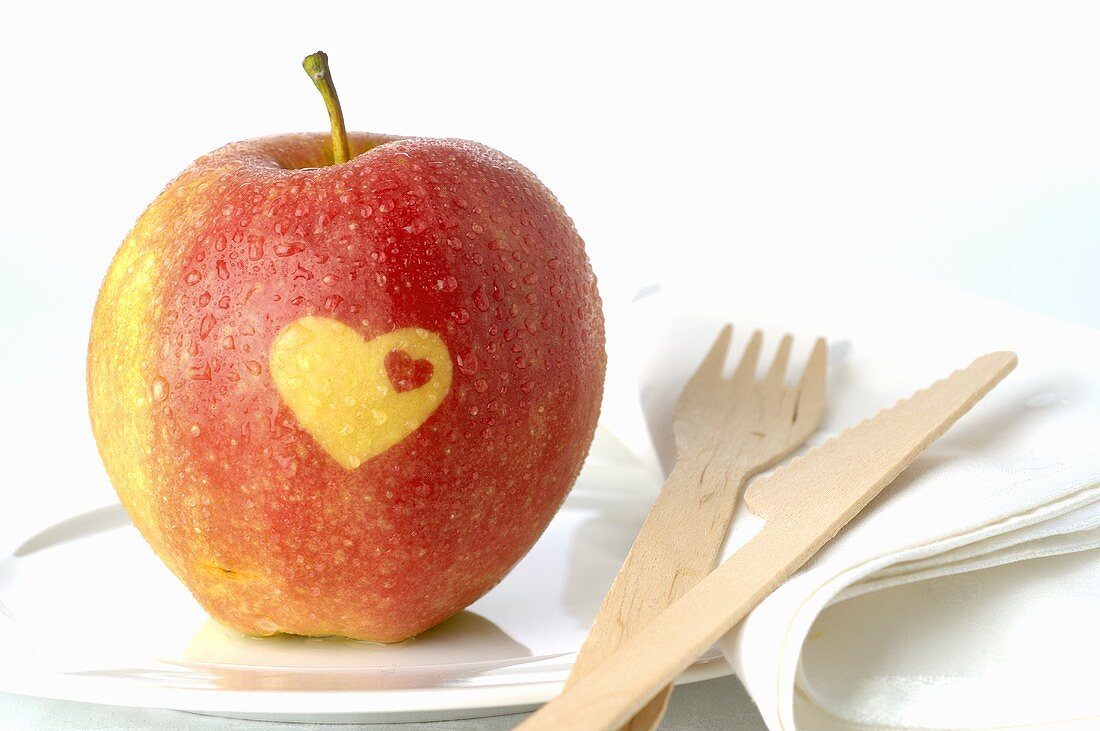 Red apple with heart on plate with wooden knife and fork