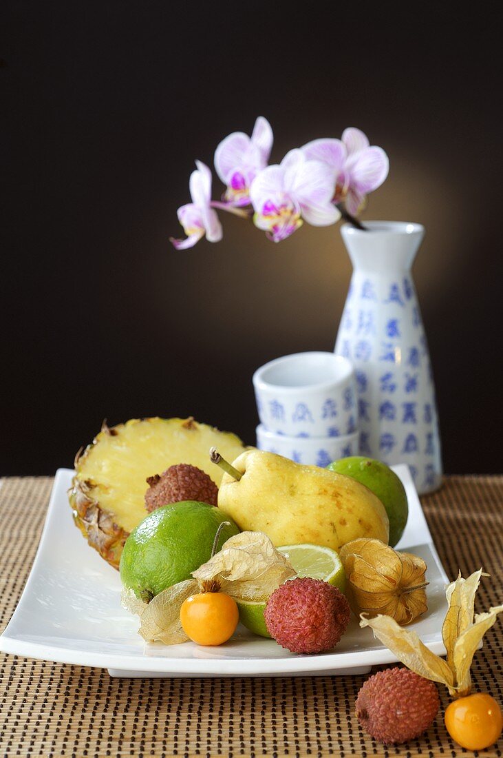 Plate of exotic fruit and orchid in vase