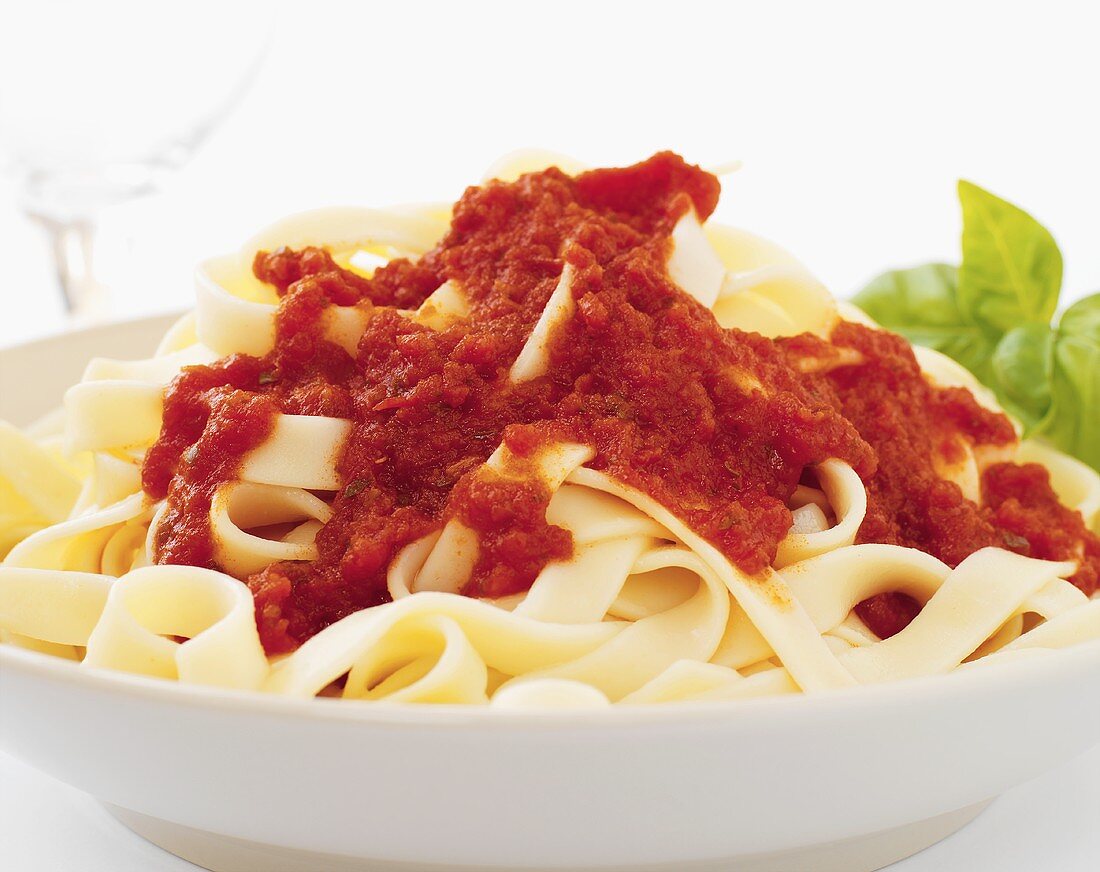 Tagliatelle with tomato sauce, basil in background