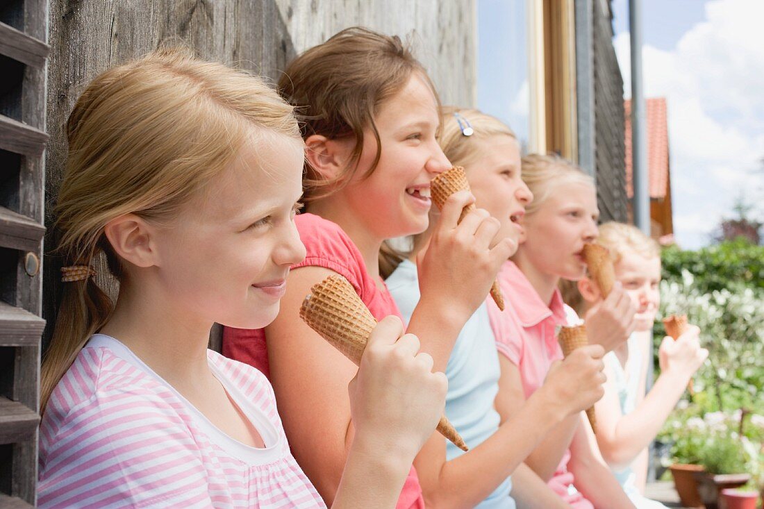 Fünf Mädchen essen Eis an einer Hauswand