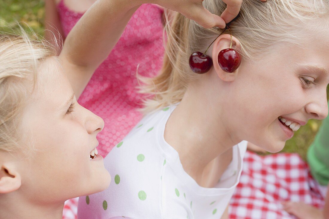 Girl hanging pair of cherries on her friend's ear