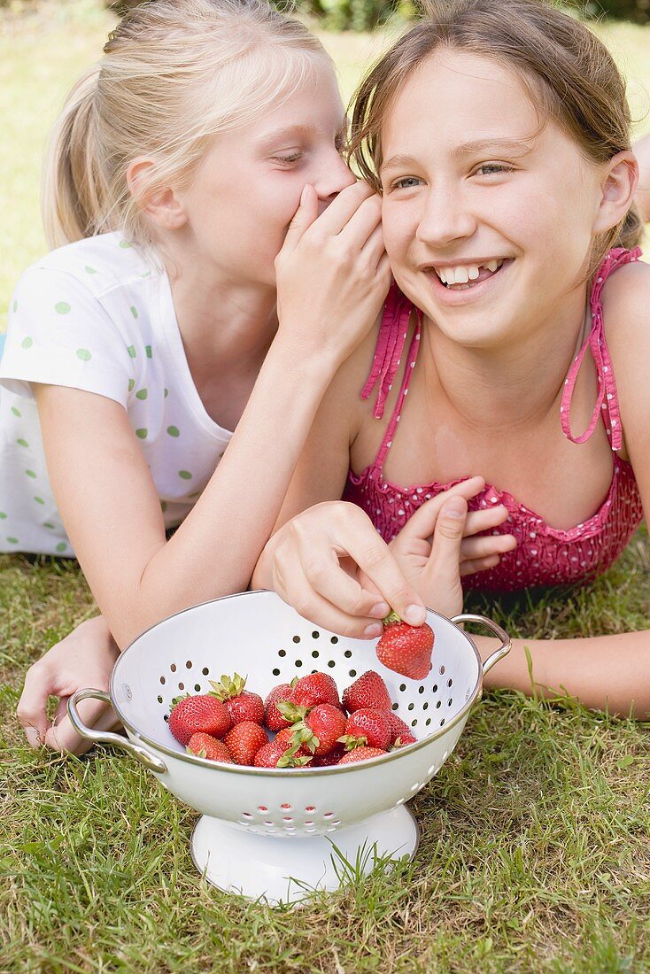 Two girls eating strawberries on grass