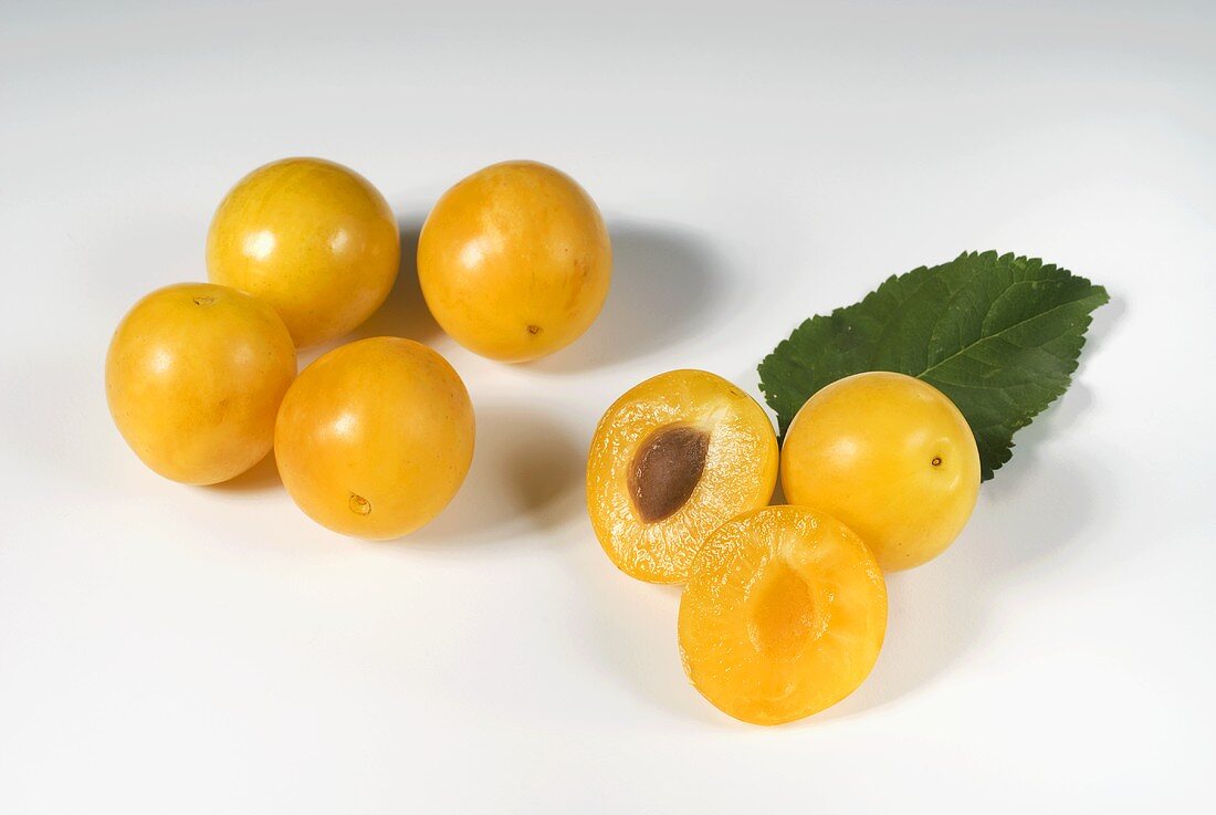 Whole and halved mirabelles with leaf