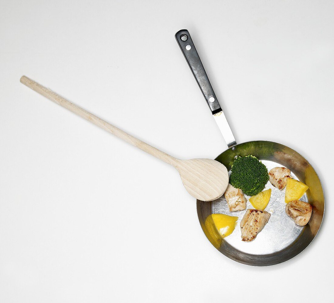 Fried chicken breast with broccoli and yellow pepper in frying pan