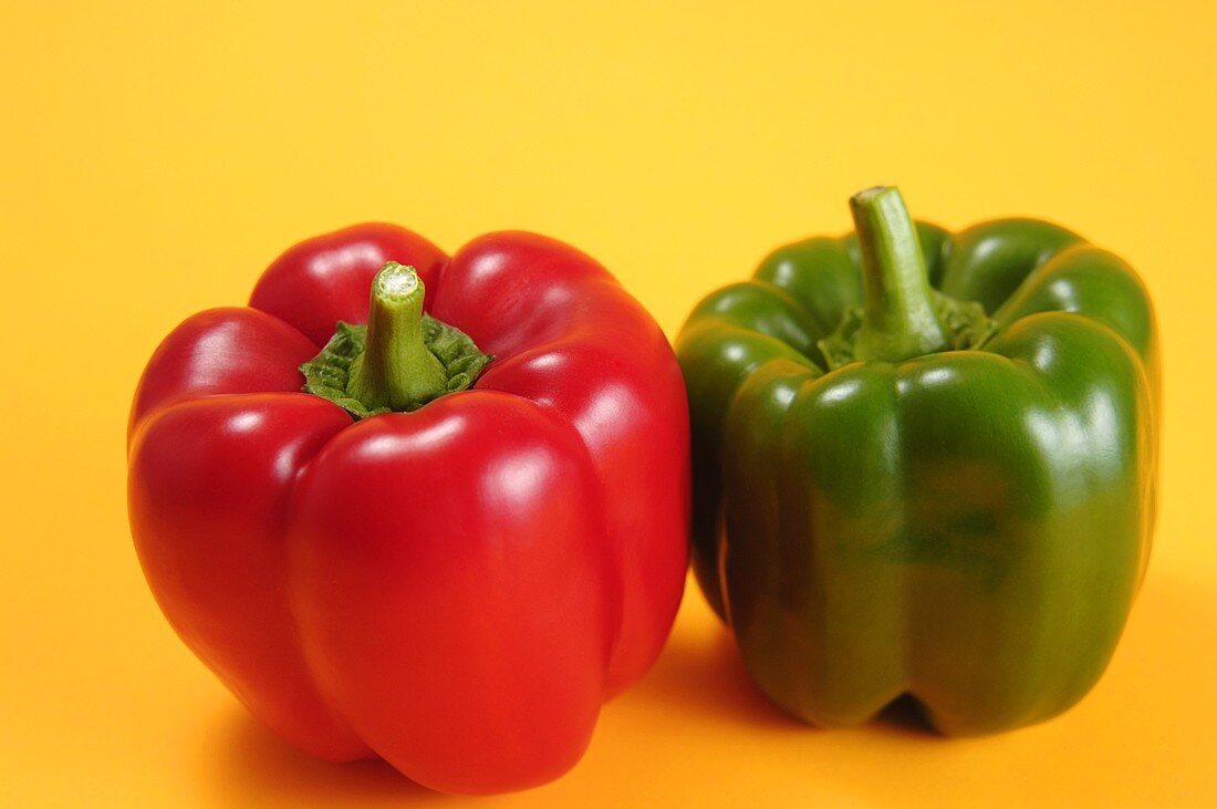 One red and one green pepper against a yellow background