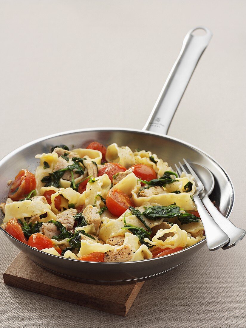 Pasta with pork, spinach and tomatoes in frying pan