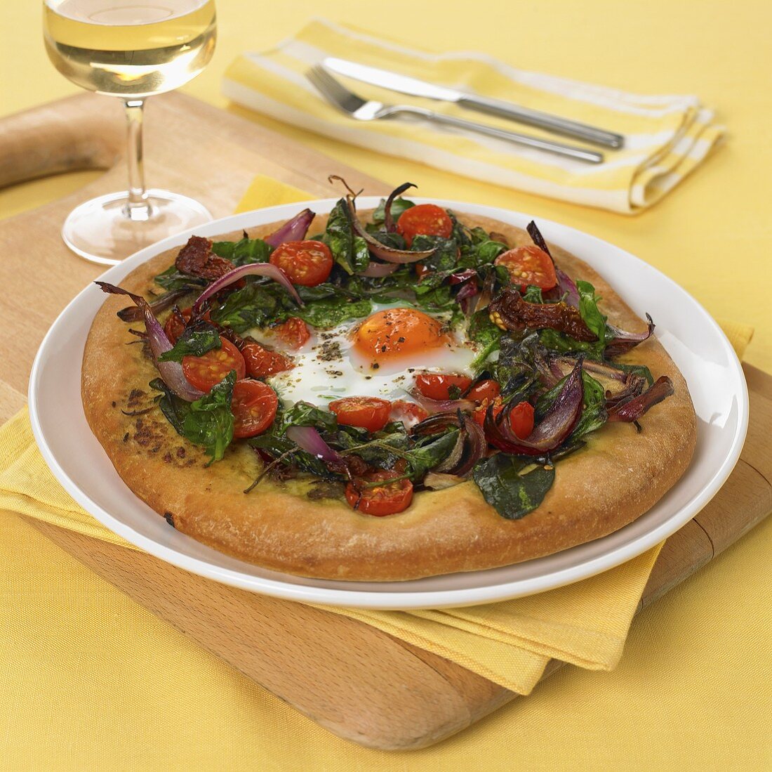 Pizza topped with fried egg, spinach, cherry tomatoes and onions