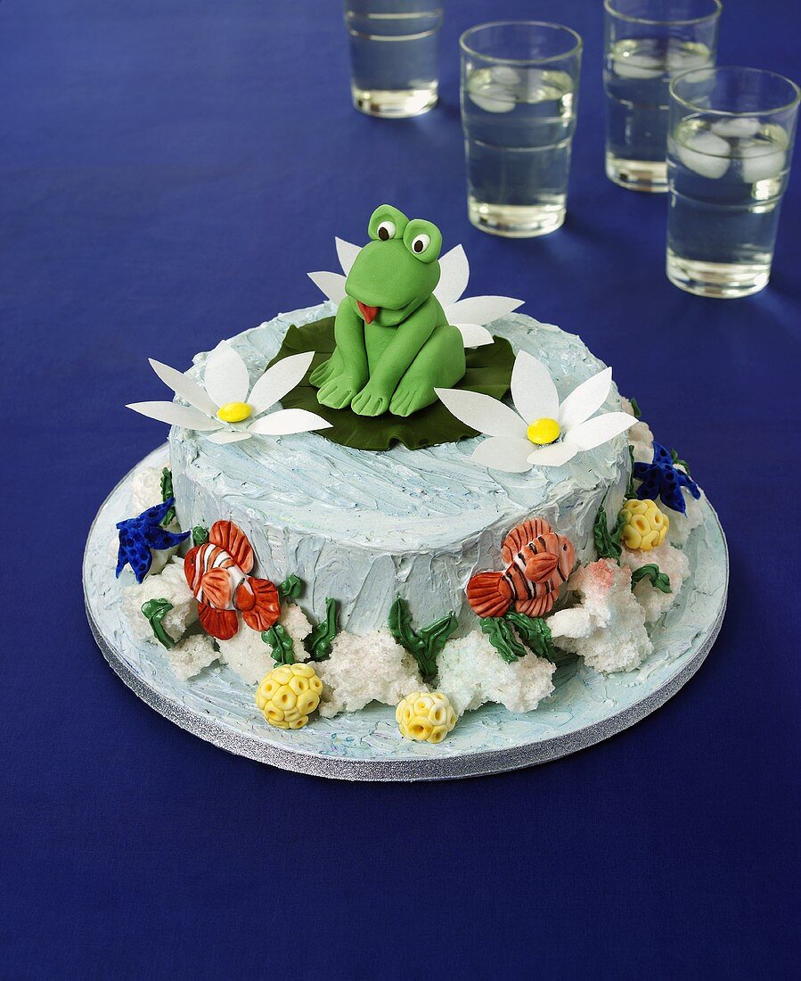 Cake decorated with frog on a lily pad, glasses of water in background