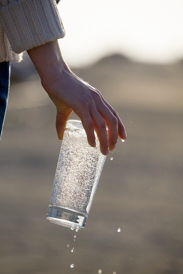 Hand hält ein Glas Mineralwasser