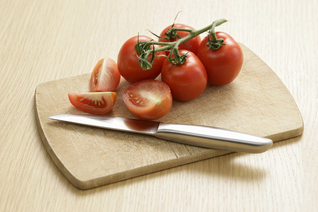 Tomatoes on the vine and a knife on a wooden board